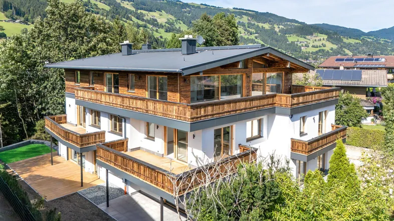 Attraktives Chalet-Gebäude mit moderner Architektur, Holzfassade, großzügigen Balkonen und Terrassen vor alpiner Bergkulisse.