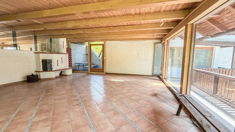 Helles, rustikales Wohnzimmer mit Holzbalkendecke, Fliesenboden und Kamin.