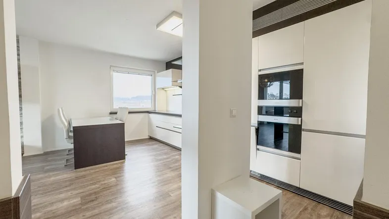 Moderne Einbauküche mit integrierten Geräten und hellem Laminatboden, offen zum Essbereich.