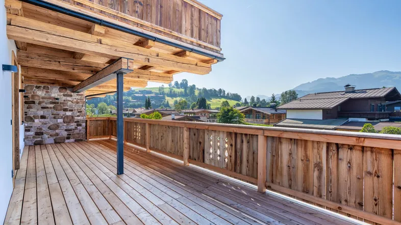 Geräumige Holzterrasse mit traditionellem Geländer und weitem Blick auf die umliegende Berglandschaft.