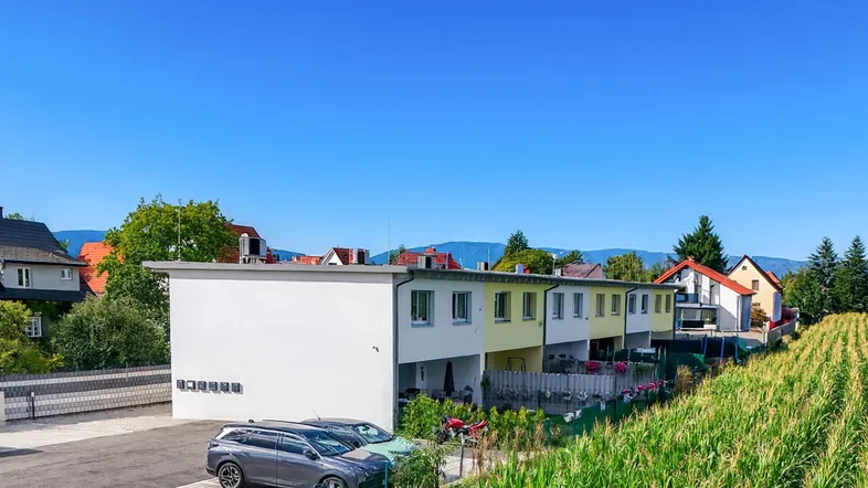 Moderne Reihenhäuser mit Parkplätzen und Blick auf ein Maisfeld und die Berge.