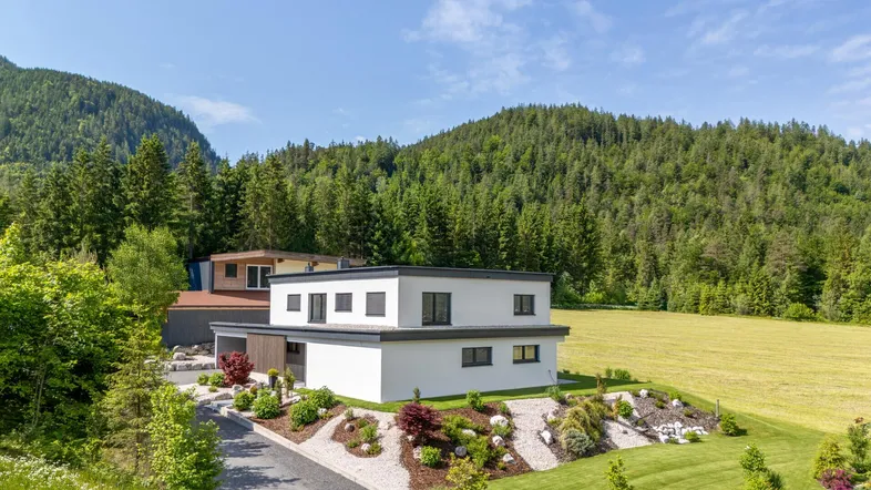 Moderne Villa in alpiner Landschaft mit gepflegtem Garten und Bergblick unter blauem Himmel.