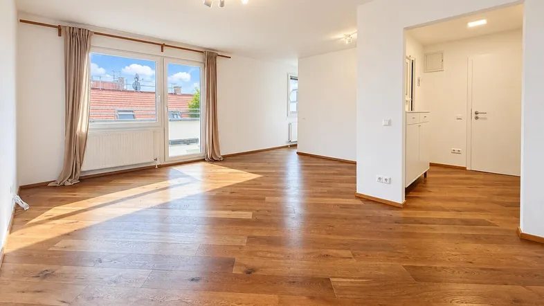 Helles Wohnzimmer mit Holzboden und Zugang zu einem Balkon oder einer Terrasse.