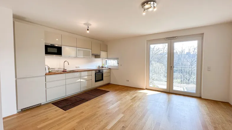 Helle Wohnküche mit modernen Schränken, Holzboden und Zugang zu einem sonnigen Balkon.