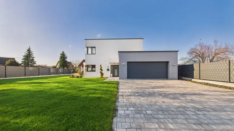 Modernes Einfamilienhaus mit Garage, gepflegtem Rasen und gepflasterter Auffahrt unter blauem Himmel.