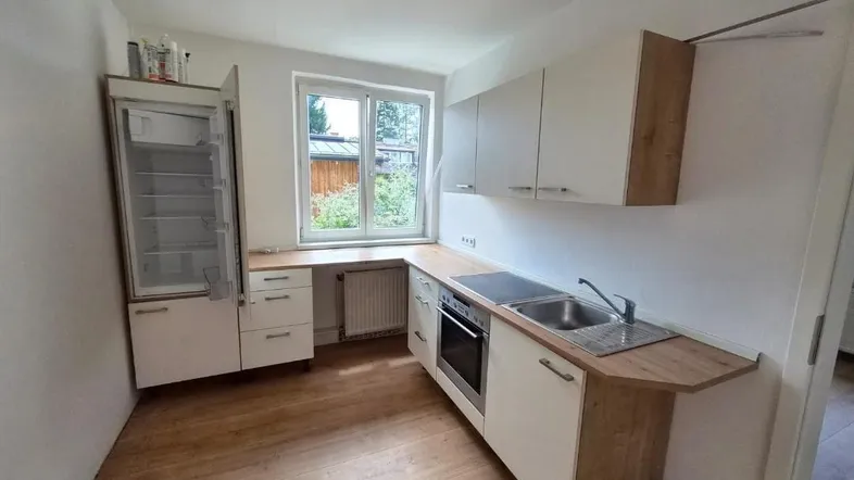 Helle Einbauküche mit Laminatboden, Fenster und integrierten Geräten, ideal für den täglichen Gebrauch.