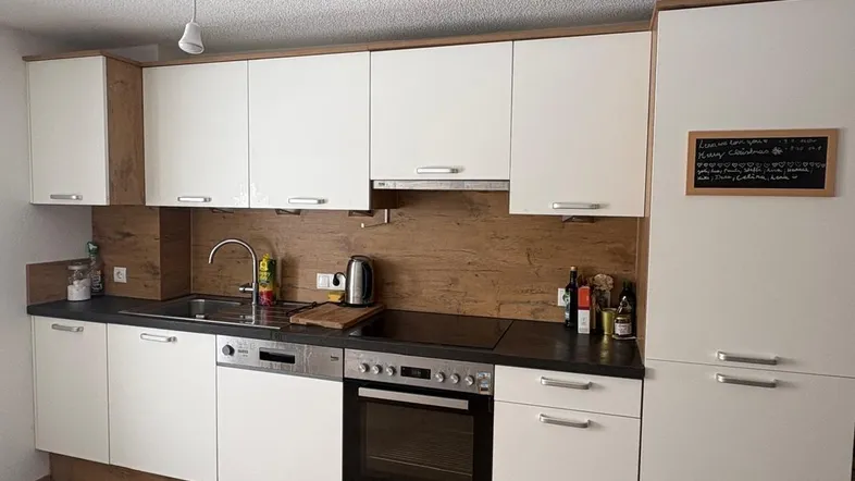 Moderne Einbauküche mit weißen Fronten, dunkler Arbeitsplatte und integrierten Geräten.