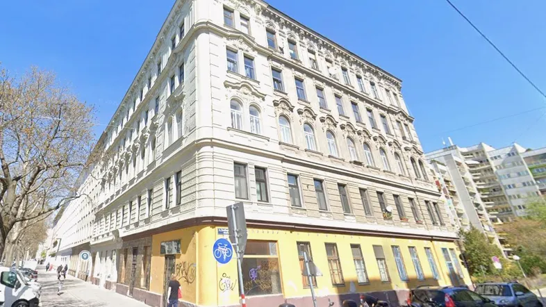 Historisches Eckgebäude mit reich verzierter Fassade in städtischer Umgebung und vielen Fenstern.