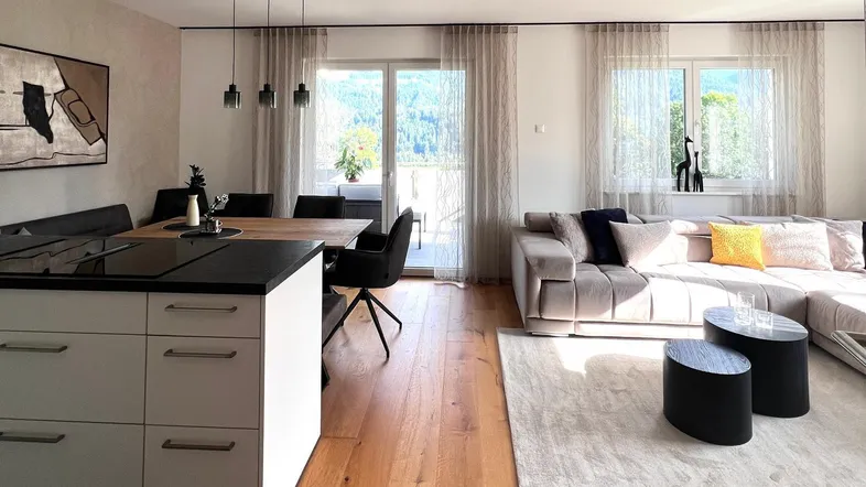 Helles, offenes Wohn-Esszimmer mit moderner Küche, Holzboden und Bergblick.