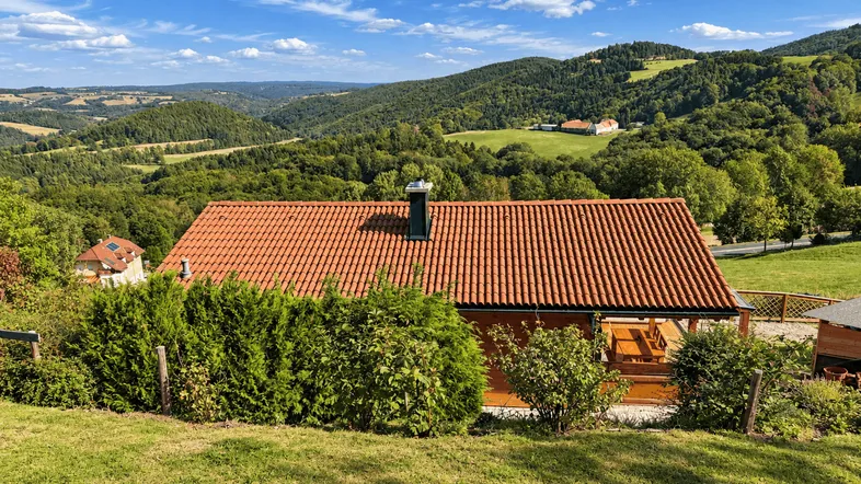 Haus mit rotem Ziegeldach in ländlicher Umgebung mit weitem Blick über grüne Hügel.