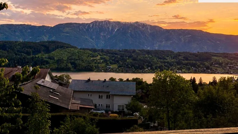 Malerischer Sonnenuntergang über dem See mit Bergblick und Häusern im Vordergrund.
