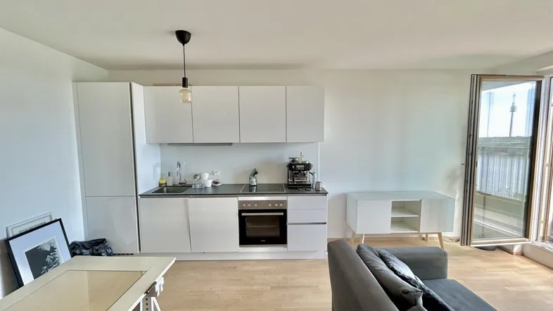 Heller offener Wohnbereich mit moderner weißer Küche, Sofa und Zugang zum Balkon mit Aussicht.