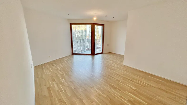 Helles Wohnzimmer mit Parkettboden und großem Fenster, das Zugang zum Balkon bietet.