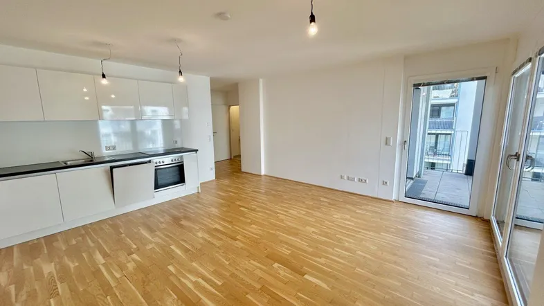 Heller offener Wohn-Essbereich mit moderner Einbauküche, Parkettboden und Zugang zum Balkon.