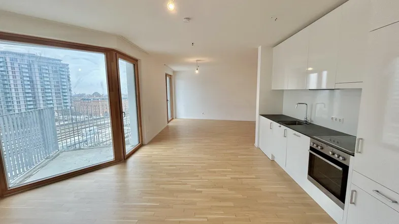 Heller offener Wohnbereich mit integrierter Küche, Parkettboden und Zugang zu einem Balkon mit Stadtblick.