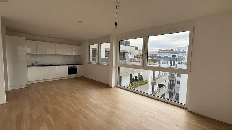 Heller offener Wohnbereich mit integrierter Küche, Parkettboden und großen Fenstern mit Stadtblick.