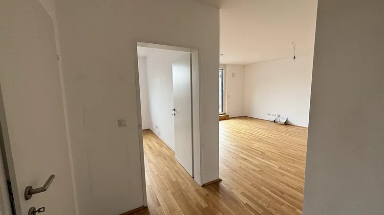 Heller Flur mit Holzboden, der in einen weiteren Raum der Wohnung führt.