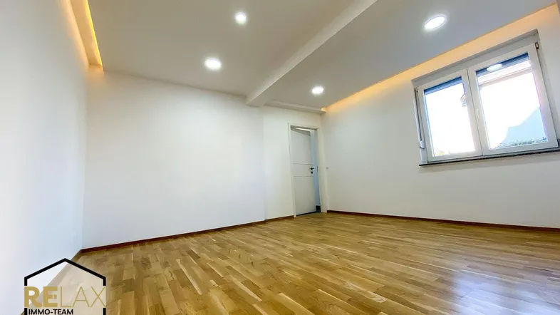 Helles, leeres Zimmer mit modernem Parkettboden und indirekter Deckenbeleuchtung, bereit zur Einrichtung.