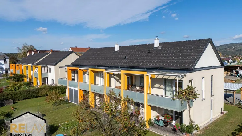 Moderne Wohnanlage mit mehreren Wohneinheiten, Balkonen und gepflegter Grünfläche unter blauem Himmel.