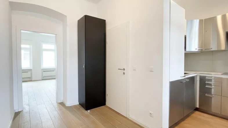 Heller Flur mit Holzboden, der zu einem weiteren Zimmer und einer modernen Küche führt.