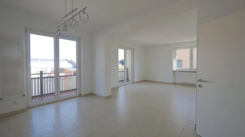 Heller, leerer Wohnbereich mit Fliesenboden und Zugang zu einem Balkon, bereit zur individuellen Gestaltung.