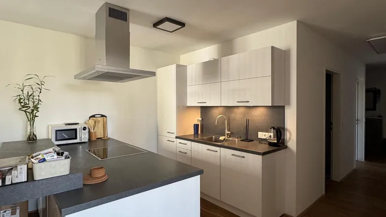 Moderne Küche mit Kochinsel, Dunstabzugshaube und Holzboden, ideal für offenes Wohnen.