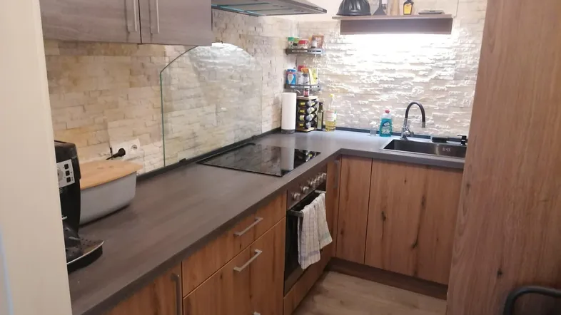 Moderne Küche mit Holzfronten, dunkler Arbeitsplatte und Steinoptik-Fliesen an der Wand.