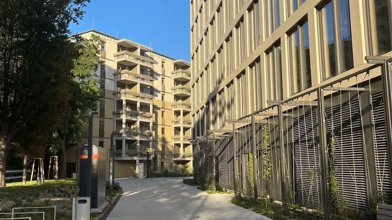 Moderner Fußweg zwischen Wohngebäuden mit Bänken und Grünflächen an einem sonnigen Tag.