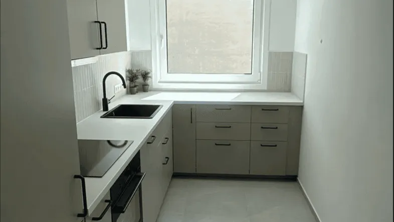Moderne Küche mit hellgrauen Schränken, weißer Arbeitsplatte, schwarzer Spüle und Induktionskochfeld.