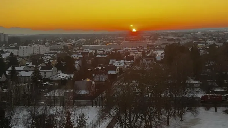 Sonnenuntergang über einer verschneiten Stadtlandschaft mit weitem Fernblick.