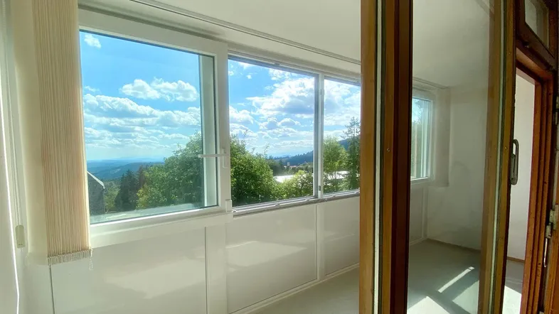 Helle Loggia mit großen Fenstern und weitem Blick über die bewaldete Landschaft.