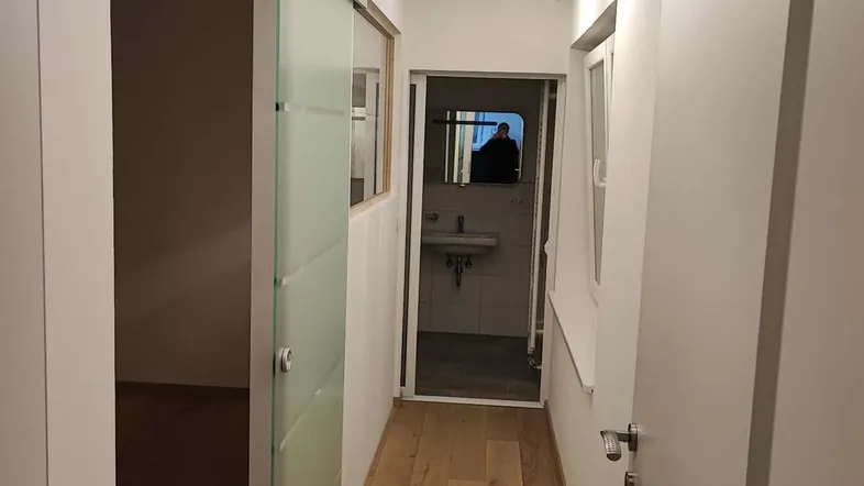 Heller Flur mit Holzfußboden, Schiebetür und Blick in ein angrenzendes Badezimmer.