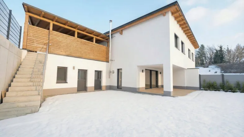 Modernes Haus mit überdachtem Holzbalkon und gepflasterter Terrasse im Schnee.
