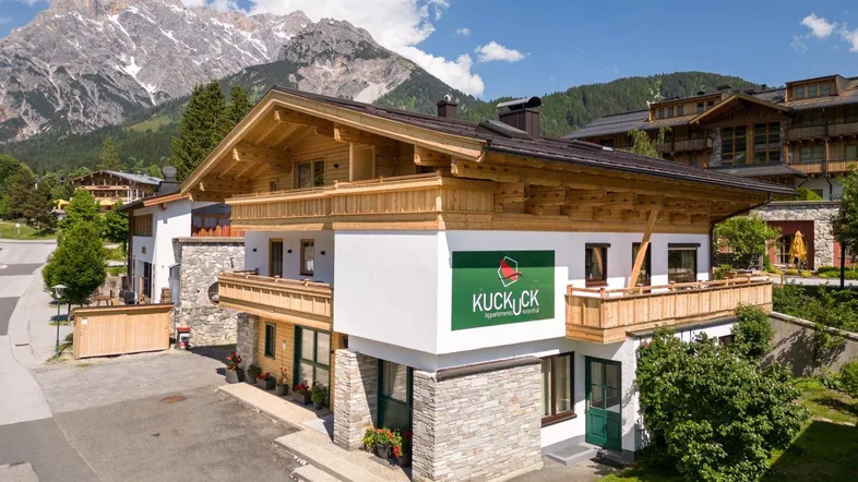 Charmantes Alpenhaus mit traditioneller Holzfassade und beeindruckendem Bergblick unter blauem Himmel.
