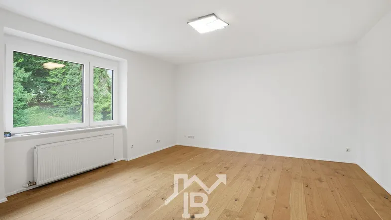 Helles Zimmer mit Holzboden und Blick ins Grüne, ideal als Wohn- oder Schlafzimmer nutzbar.