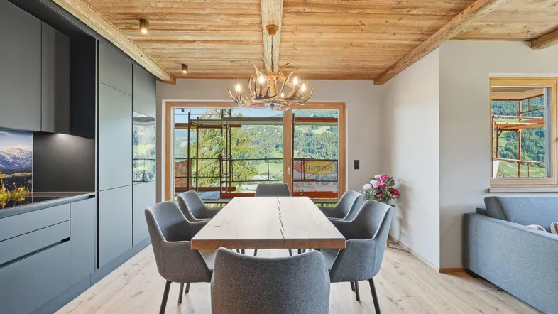Moderner offener Wohn-Essbereich mit Holzbalkendecke, grauer Küche und Bergblick.