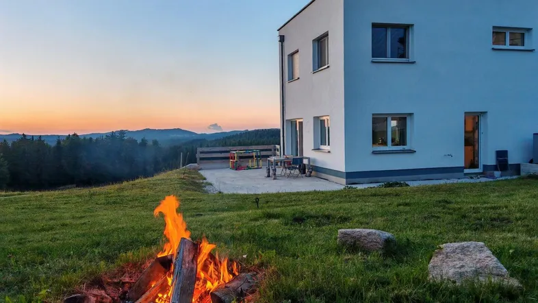 Modernes Haus bei Sonnenuntergang mit Lagerfeuer im Garten und weitem Blick in die Landschaft.