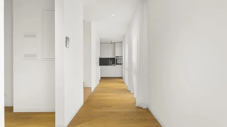 Heller Flur mit modernem Holzparkettboden, der zu einer minimalistischen Küche führt.