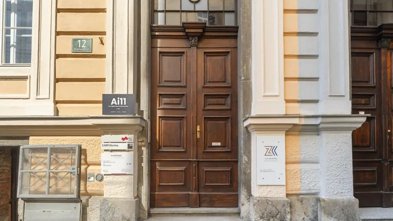Detailansicht des Haupteingangs mit einer verzierten Holztür und Hinweisschildern an der Fassade.
