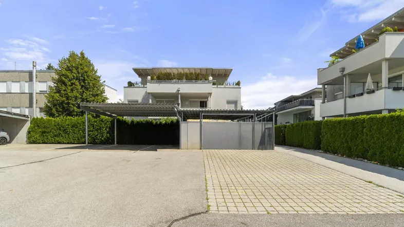 Moderne Wohnanlage mit Carport und gepflegter Außenanlage unter blauem Himmel.