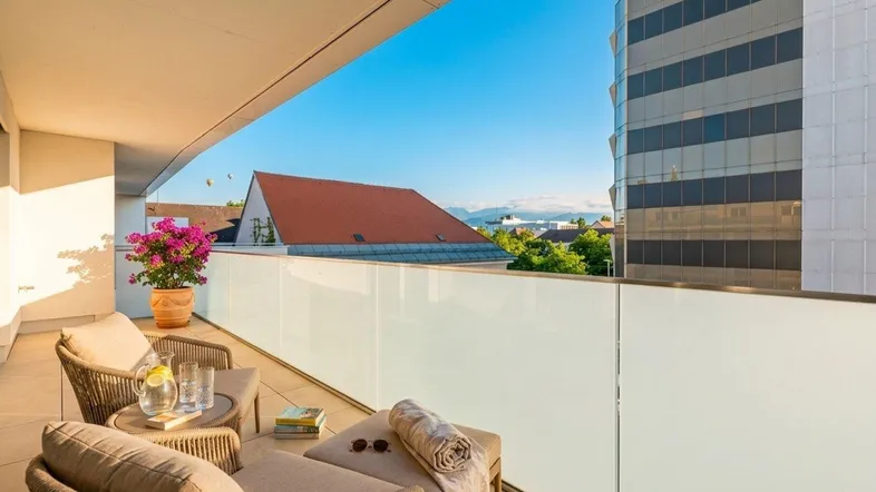Sonniger Balkon mit bequemen Loungemöbeln und Blick auf die Stadt sowie die Berge.