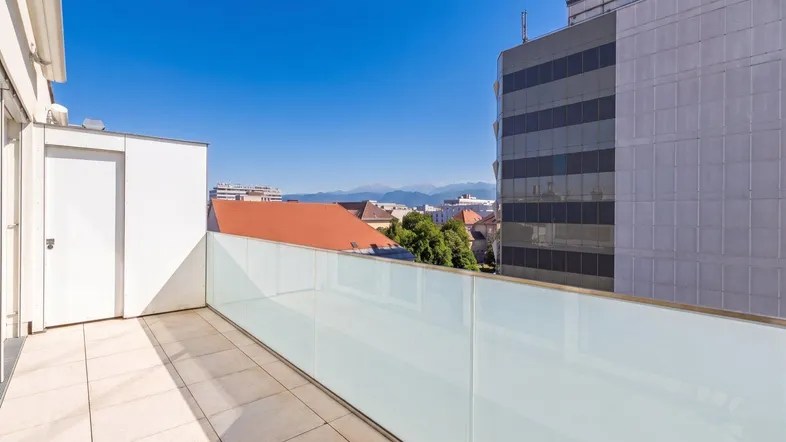 Heller Balkon mit moderner Glasbrüstung, Fliesenboden und weitem Blick über die Stadt bis zu den Bergen.