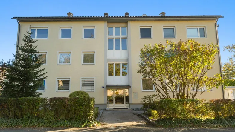 Vorderansicht eines Mehrfamilienhauses mit gepflegter Fassade und umgebenden Grünflächen.