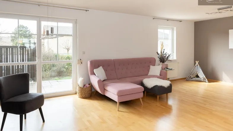 Helles Wohnzimmer mit Holzboden, rosa Sofa und Zugang zum Gartenbereich.