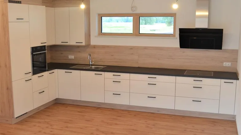 Moderne Einbauküche mit hellen Fronten, dunkler Arbeitsplatte und Laminatboden in einem offenen Raum.