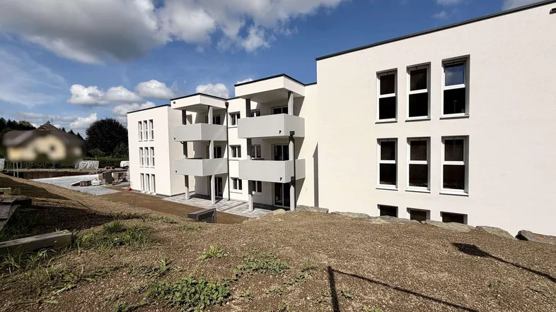 Modernes Mehrfamilienhaus mit weißer Fassade und Balkonen, umgeben von einer Baustelle.
