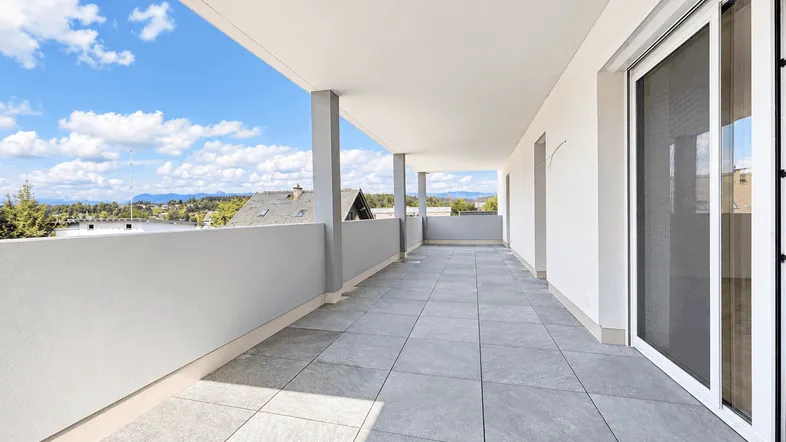Geräumige Terrasse mit Fliesenboden und weitem Blick über die Dächer und Landschaft.