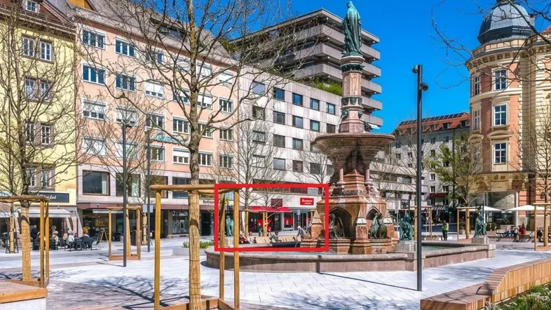 Städtischer Platz mit Brunnen und umliegenden Gebäuden, das Objekt ist rot markiert.