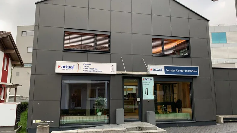 Modernes Geschäftsgebäude mit dunkler Fassade, großen Schaufenstern und Jalousien im Obergeschoss.