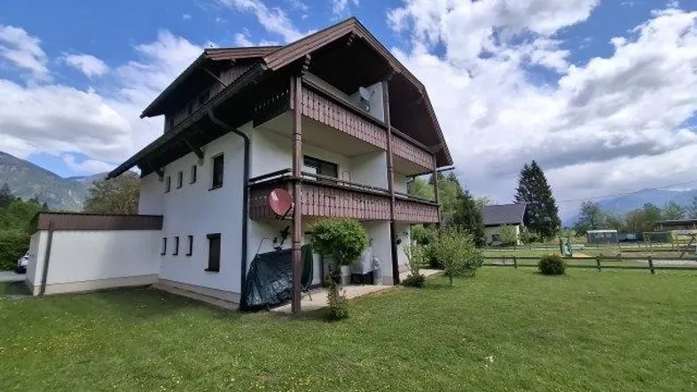 Traditionelles Haus mit mehreren Holzbalkonen, umgeben von einer grünen Wiese und Bergblick.